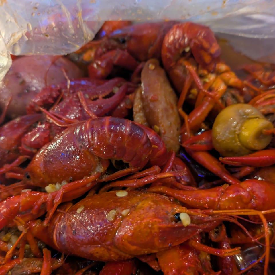 Boiled crawfish, sausage, corn, and potatoes in a clear plastic bag.