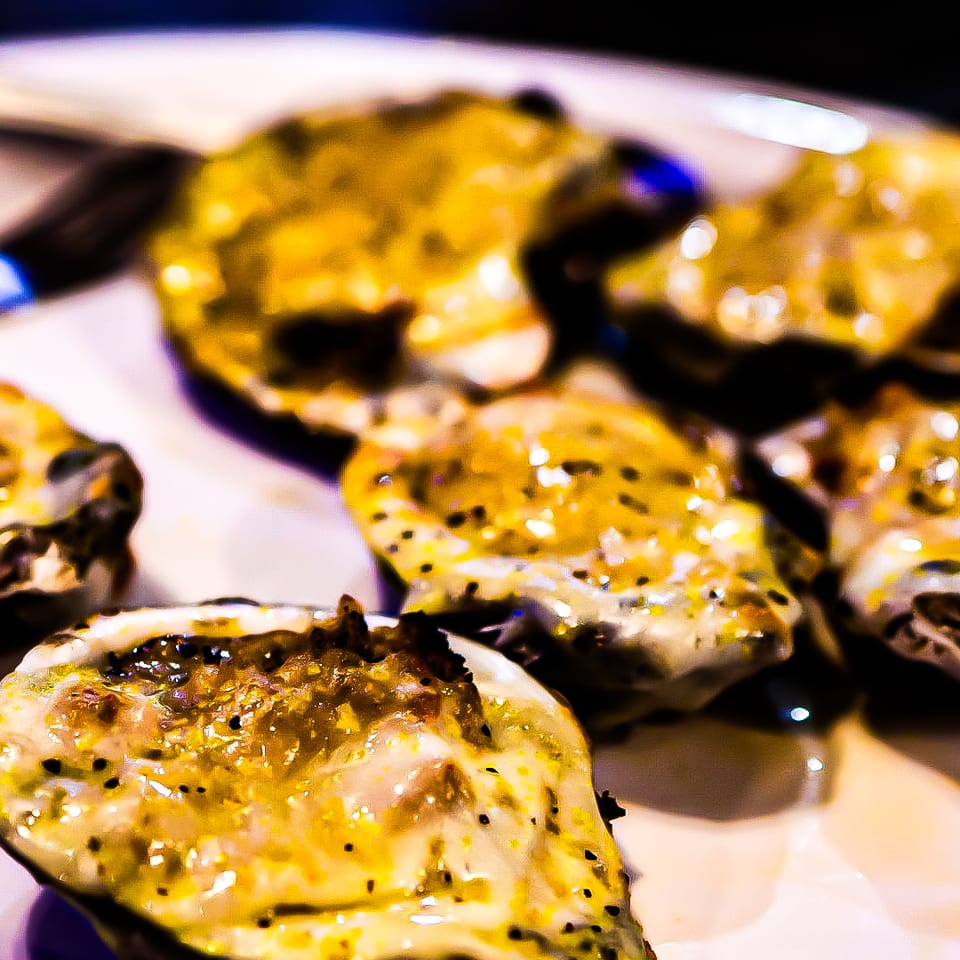 Close-up of baked oysters with melted cheese and black pepper on a white plate.