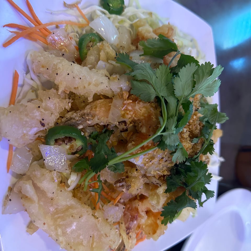 Crispy fried shrimp and vegetables, including cabbage, carrots, jalapeños, and cilantro, on a white plate.