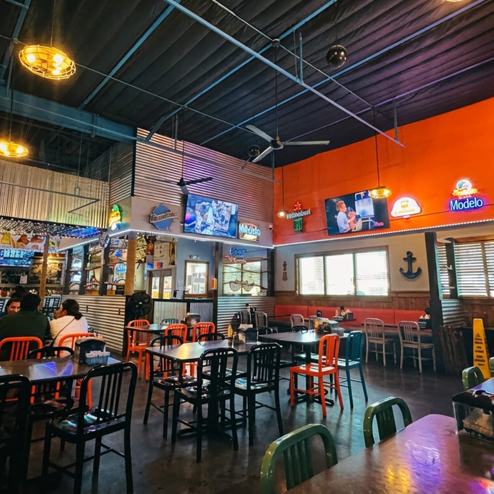 Spacious restaurant interior with high ceilings, multiple tables, and an orange accent wall with neon signs.