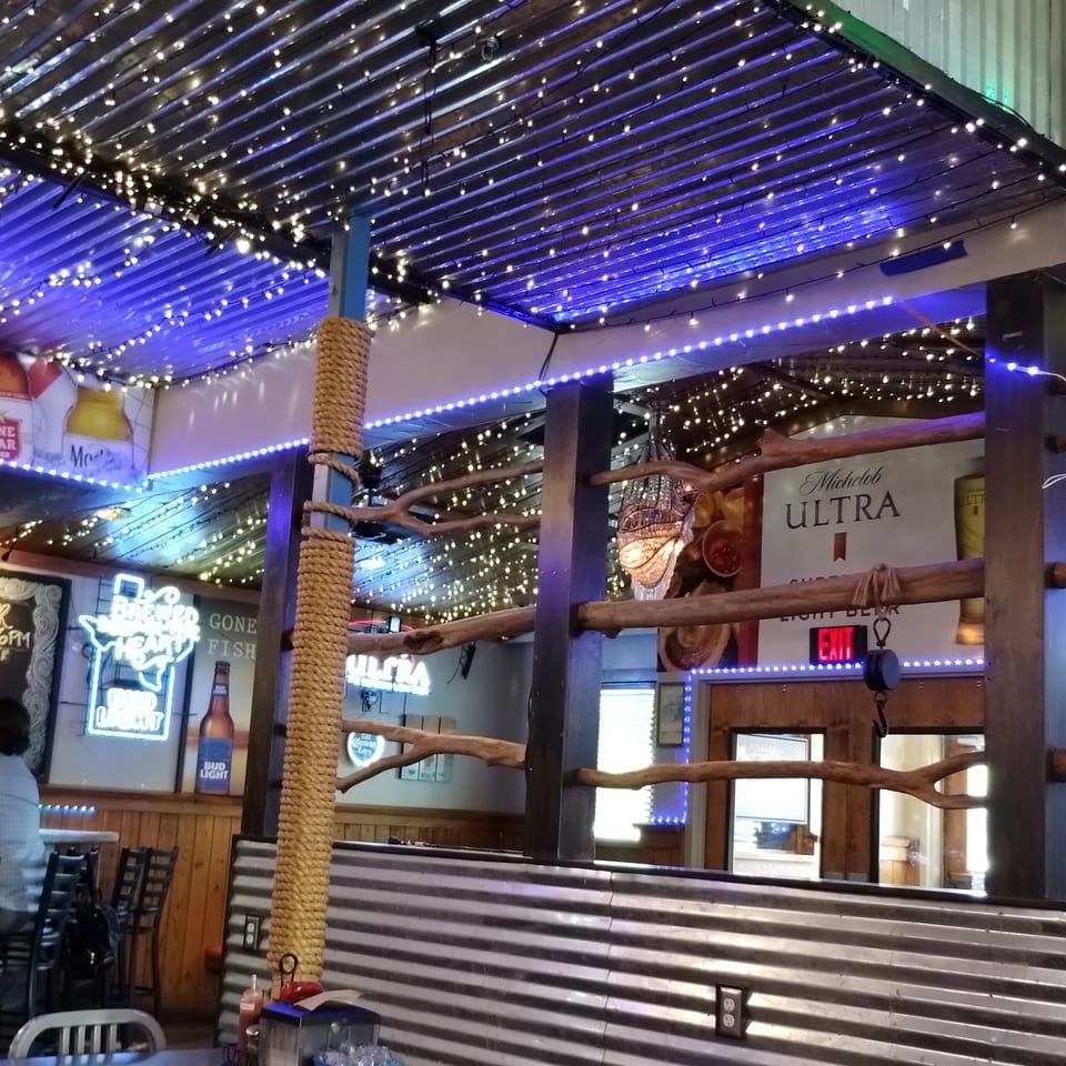 Restaurant interior with string lights on a corrugated metal ceiling, neon signs, and metal chairs.