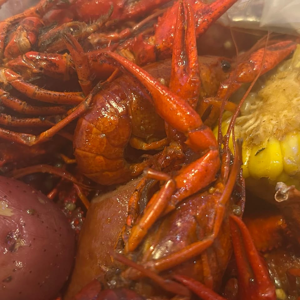 Boiled crawfish, corn on the cob, and a red potato in a clear plastic bag.