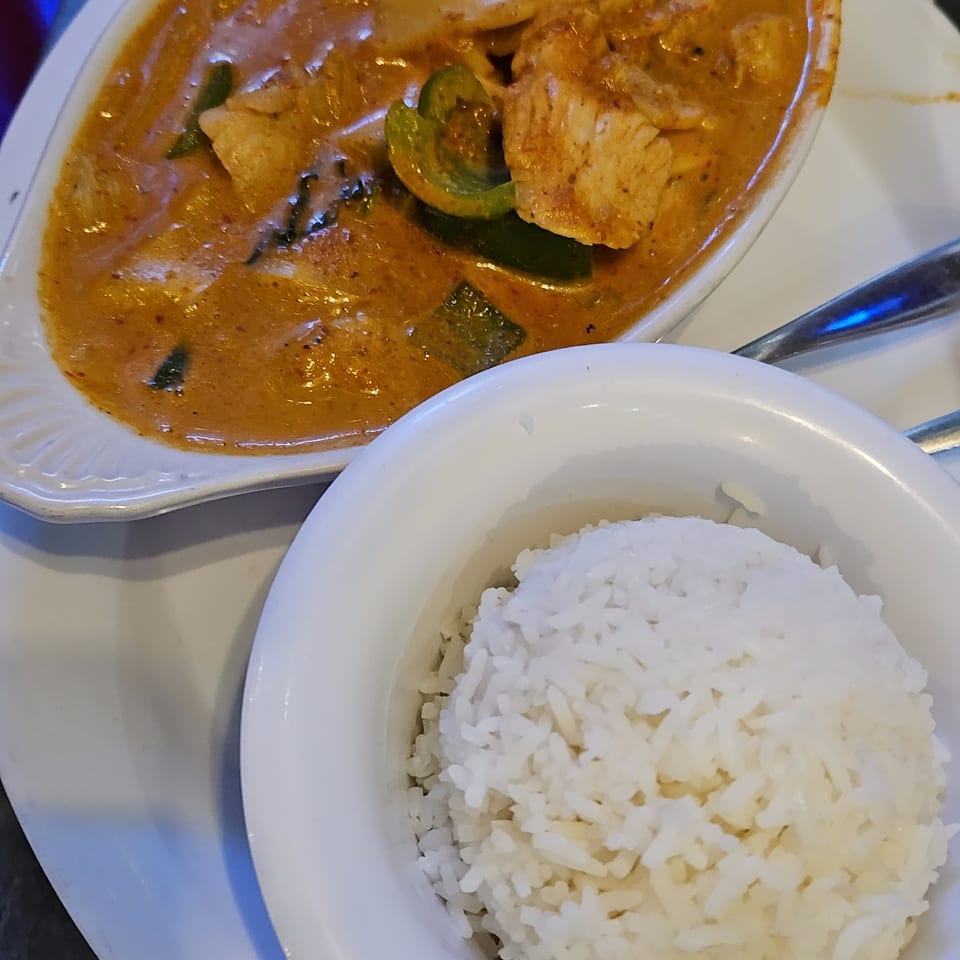 A bowl of red curry with chicken and green peppers, served with a side of white rice.