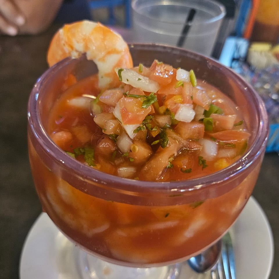Shrimp cocktail in a glass with pico de gallo, garnished with a large shrimp.