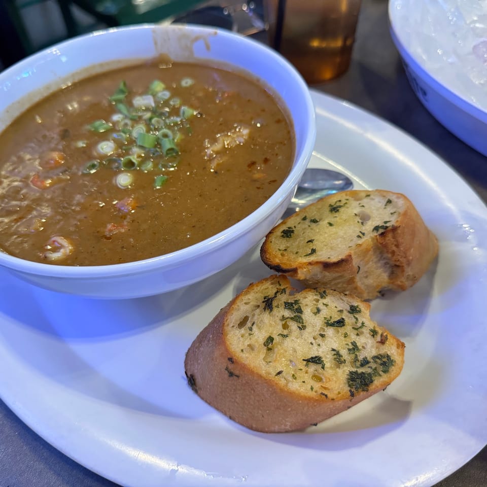 A bowl of gumbo with green onions and two slices of garlic bread on a white plate.
