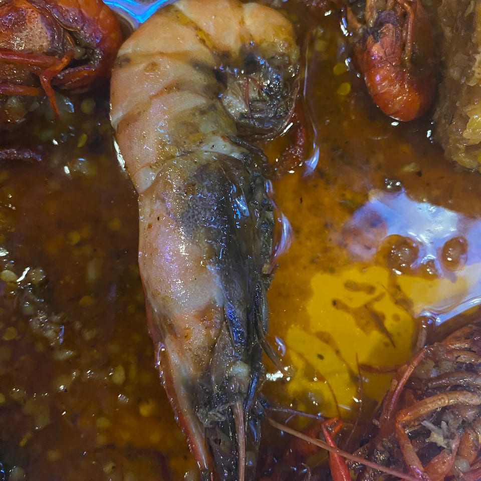Close-up of a large shrimp and several crawfish in a rich, spicy sauce.