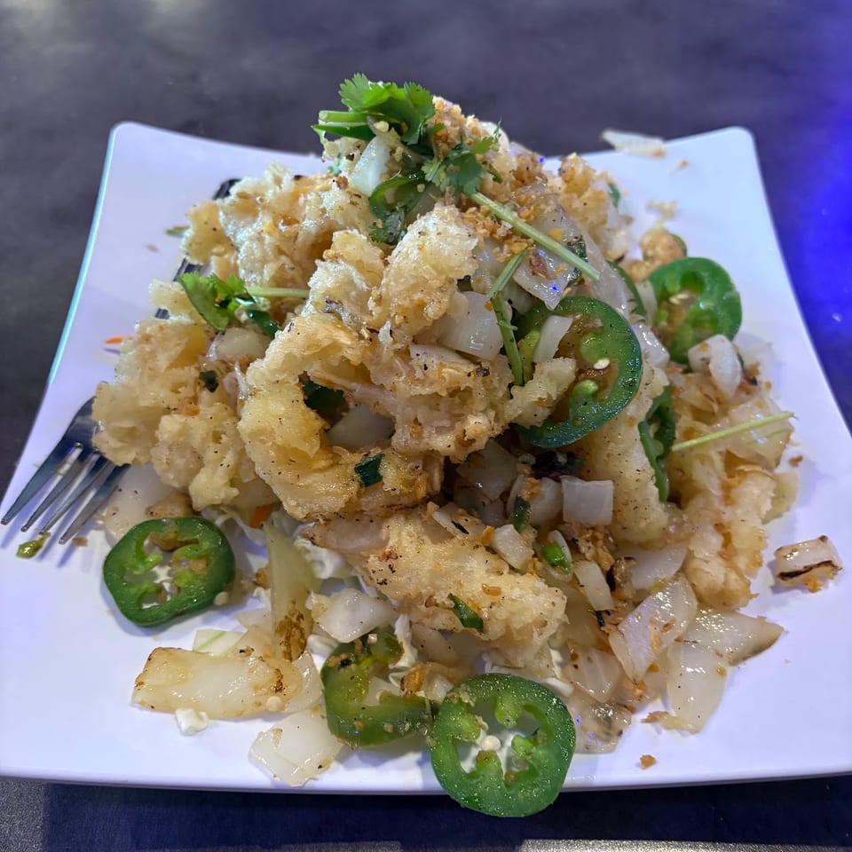 Crispy fried calamari with sliced jalapeños, onions, and cilantro on a white plate.