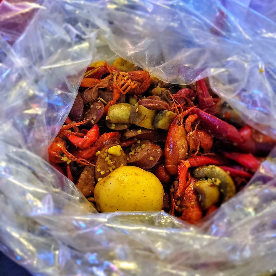 Boiled crawfish, sausage, mushrooms, and a potato in a clear plastic bag.