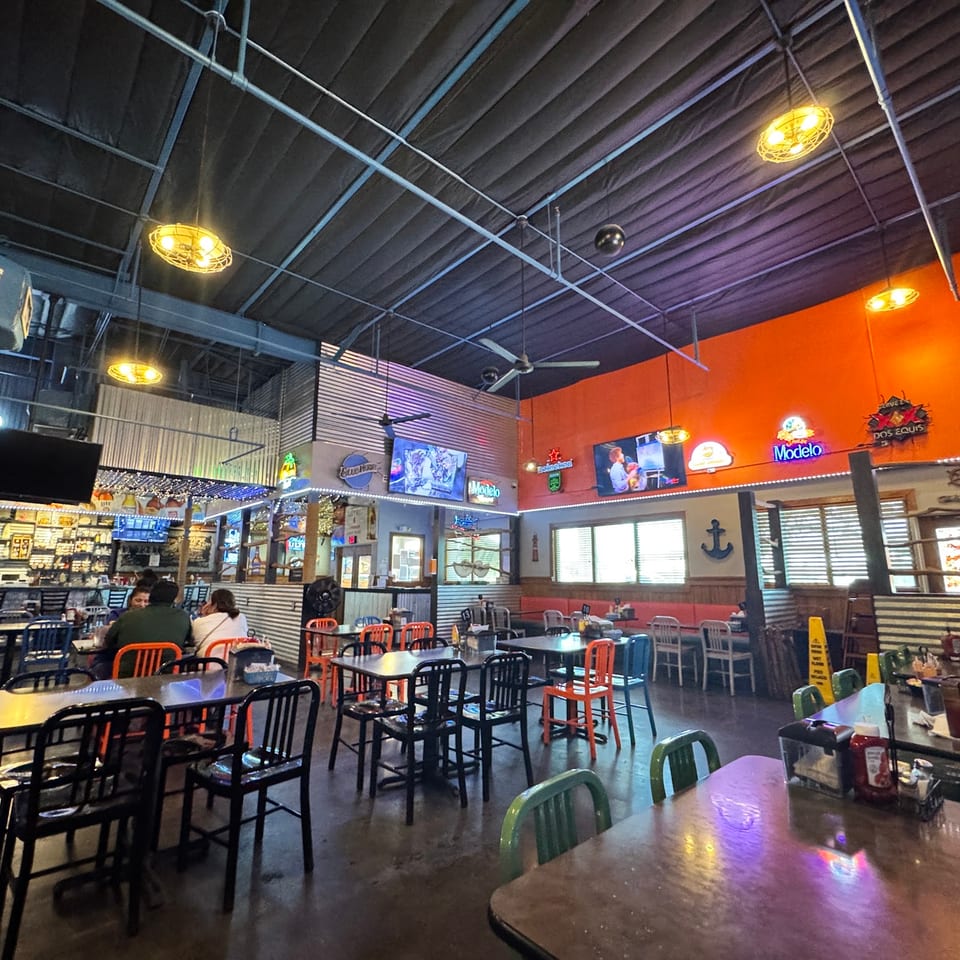 Spacious restaurant interior with orange walls, exposed ceiling, colorful chairs, and a few patrons dining.