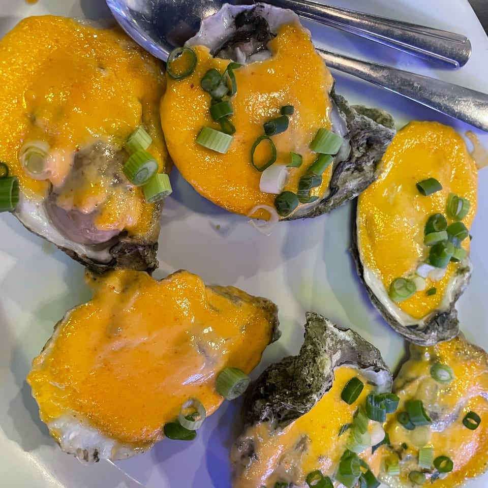 Baked oysters topped with melted cheese and green onions, served on a white plate with spoons.