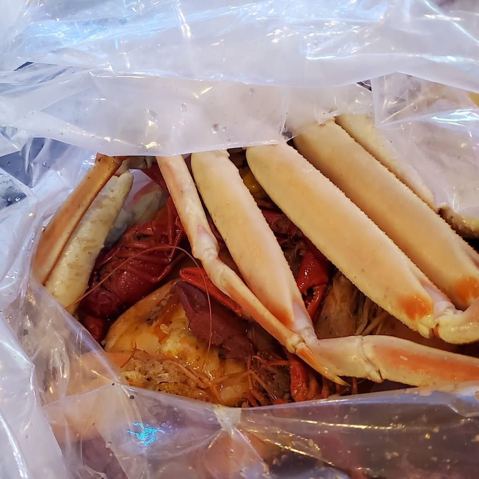 A plastic bag filled with a seafood boil including snow crab legs, crawfish, and shrimp.