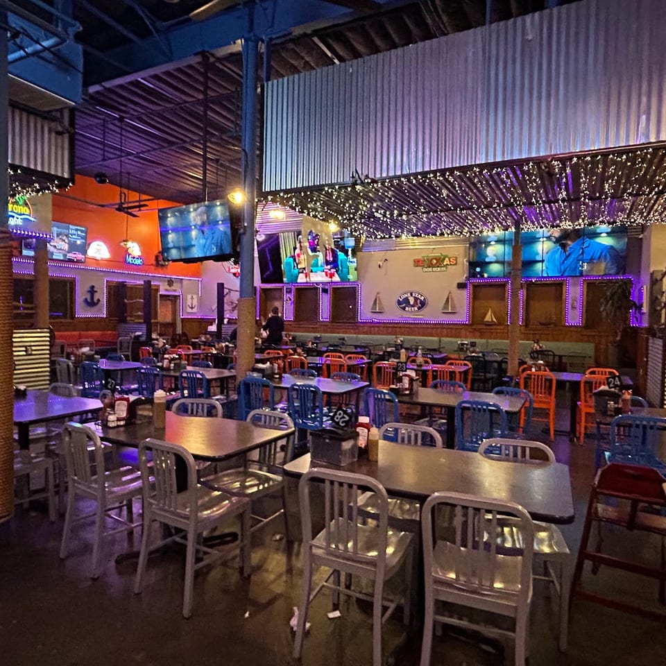 Spacious restaurant interior with numerous tables and chairs, illuminated by string lights and purple accents.