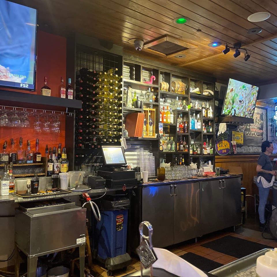 A restaurant bar with bottles of liquor, wine racks, beer taps, and a bartender working.